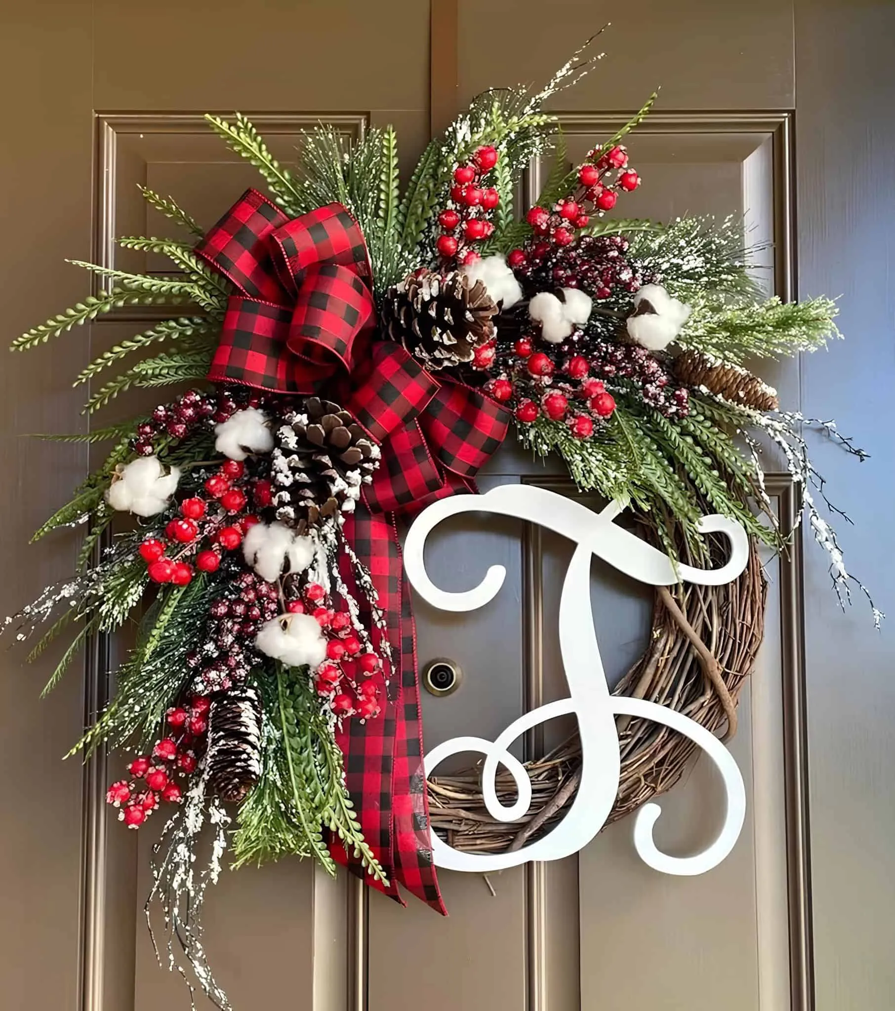 Monogramm-Buffalo-Plaid-Kopfkissen aus Baumwolle sowie Holzkranz mit Beeren Holzkranz in Form eines Rebenrankens mit Monogramm, Schleife im Buffalo-Plaid-Stil, Baumwollkapseln, Kiefernzapfen und roten Beeren