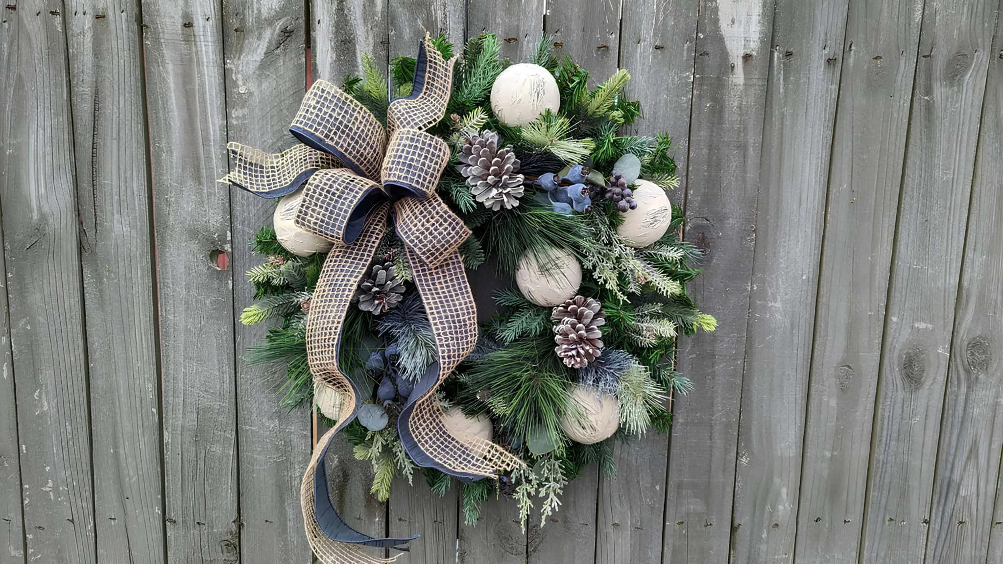 Rustikaler Kiefernkränzchen mit neutralen Verzierungen, getönten Kiefernzapfen und blauer Schleife Rustikales Kiefernkränzchen mit neutralen Ornamenten, getönten Zapfen und blauer Schleife
