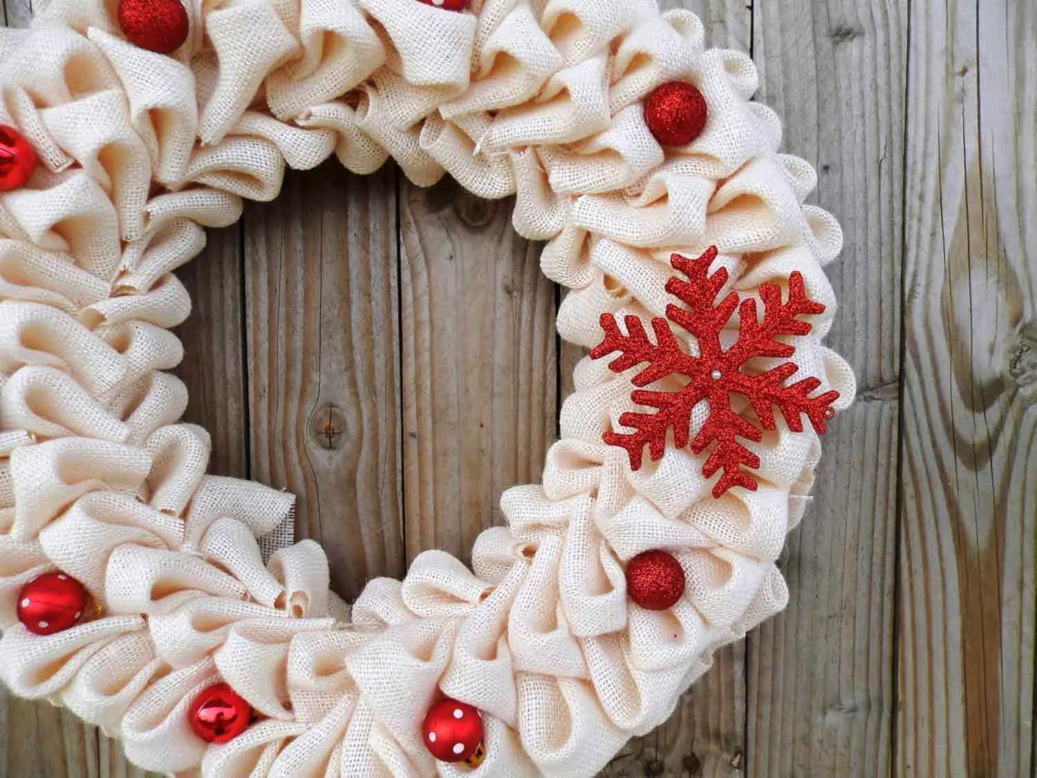Roter Schneeflocken-Krem-Jute-Kranz Festlicher Stoff-Weihnachtskranz mit roten Verzierungen und einer roten Schneeflockendekoration auf einem rustikalen Holzgrund.