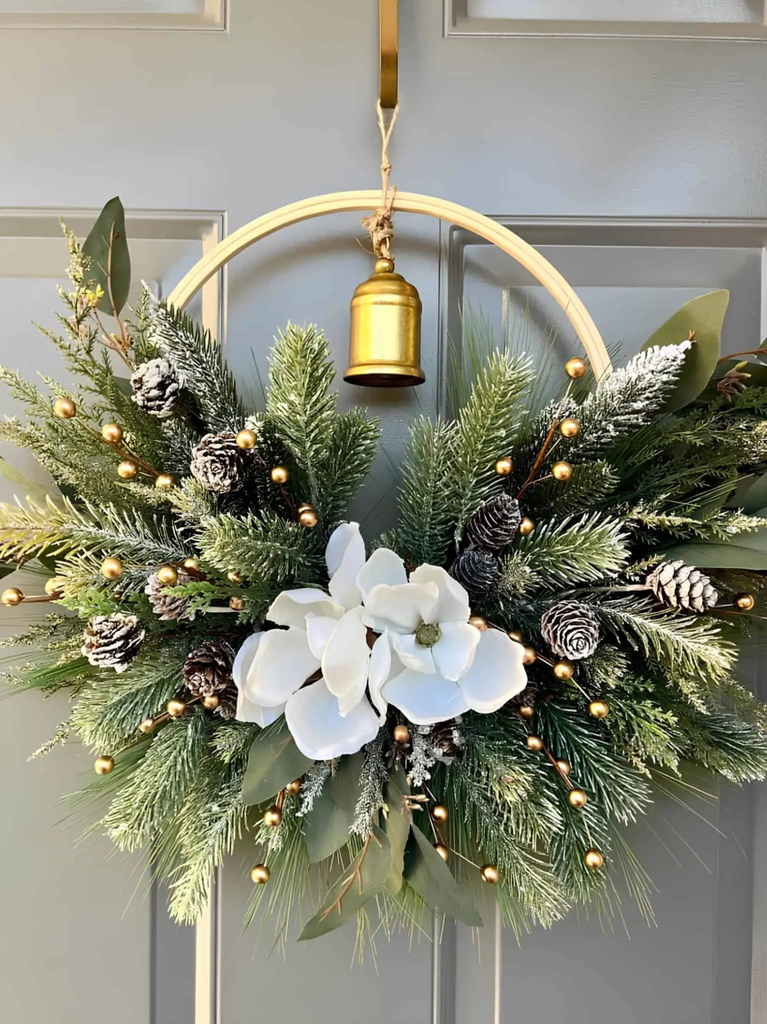 Weihnachtskranz mit Magnolien und Glocken Eleganter Weihnachtskranz mit Magnolienblüten, bemalter Kiefer und einer goldenen Glocke