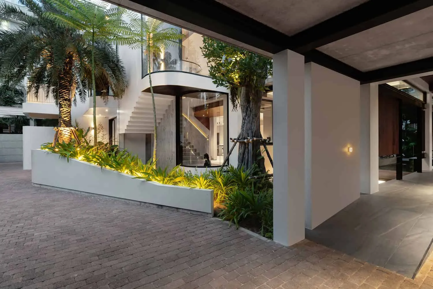 Abendlicher Eingangsbereich des Wat Bo House mit skulpturaler Treppe und Landschaftsbeleuchtung von UAD Architects Wat Bo House von UAD Architects – Abendlicher Eingangsbereich mit skulpturaler Treppe und Landschaftsbeleuchtung in Kambodscha