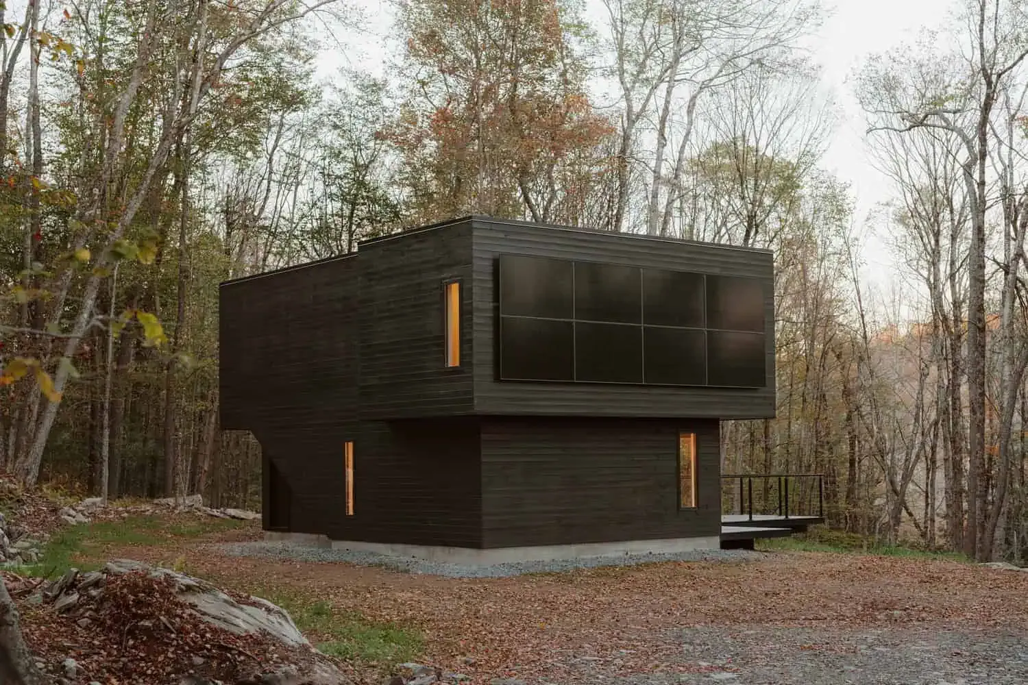 Ein zeitgenössisches, schwarzes modernes Haus in einem Waldgebiet mit ansprechendem Design und großen Fenstern, das innovative Architektur sowie umweltfreundliche Materialien in einer bewaldeten Umgebung zeigt.